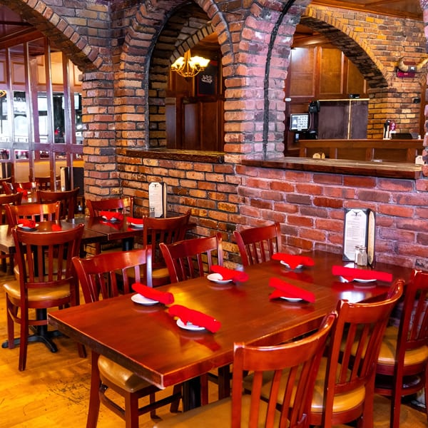 Warm, inviting dining room at 354 Steakhouse with brick arches, wooden tables, and red napkins.