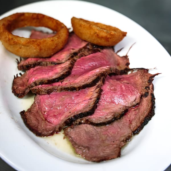 Sliced medium-rare steak with two golden onion rings and a potato wedge on a white plate.