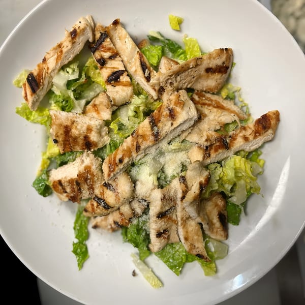 Grilled chicken Caesar salad with parmesan cheese on a white plate at 354 Steakhouse.