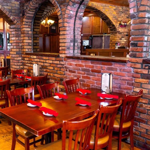 Warmly lit 354 Steakhouse dining room with brick arches, wooden tables, and red napkins.