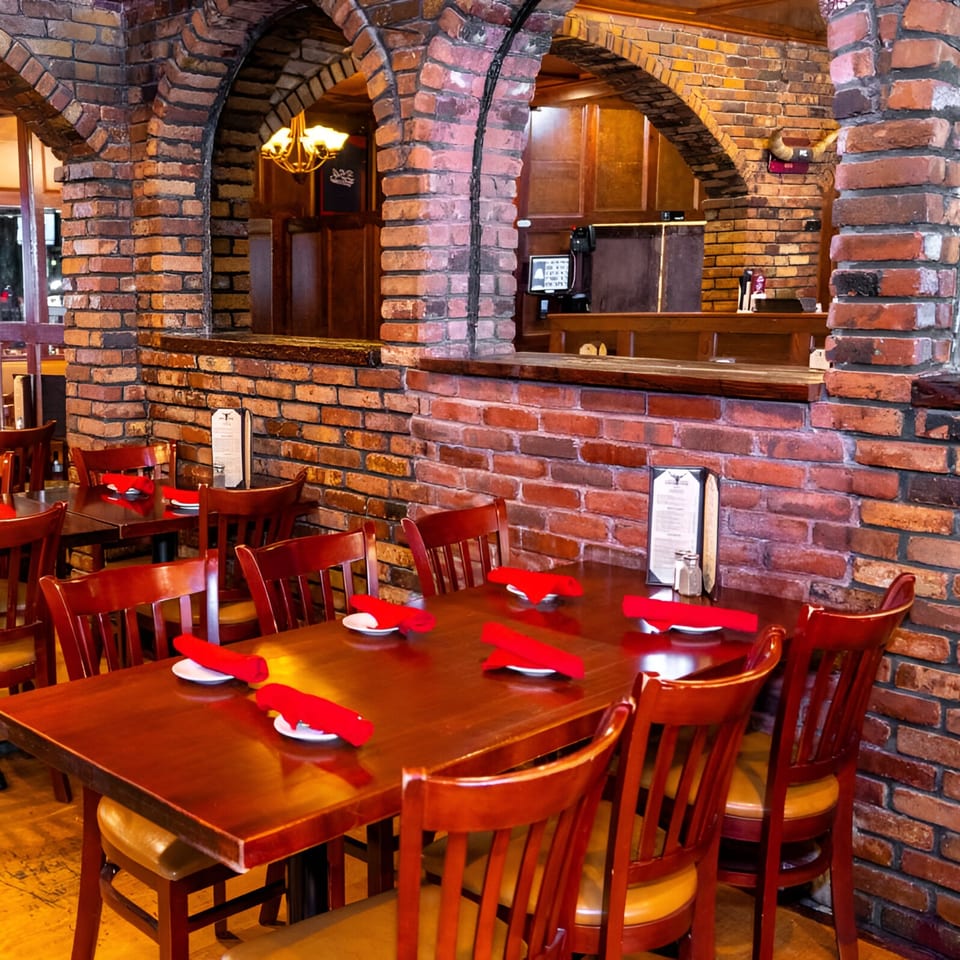 Warmly lit 354 Steakhouse dining room with brick arches, wooden tables, and red napkins.