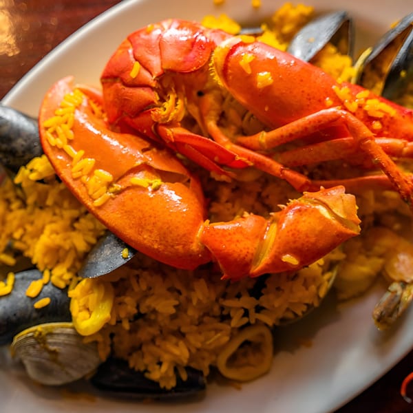 Close-up of a vibrant paella with a whole lobster, mussels, and clams on a white plate.