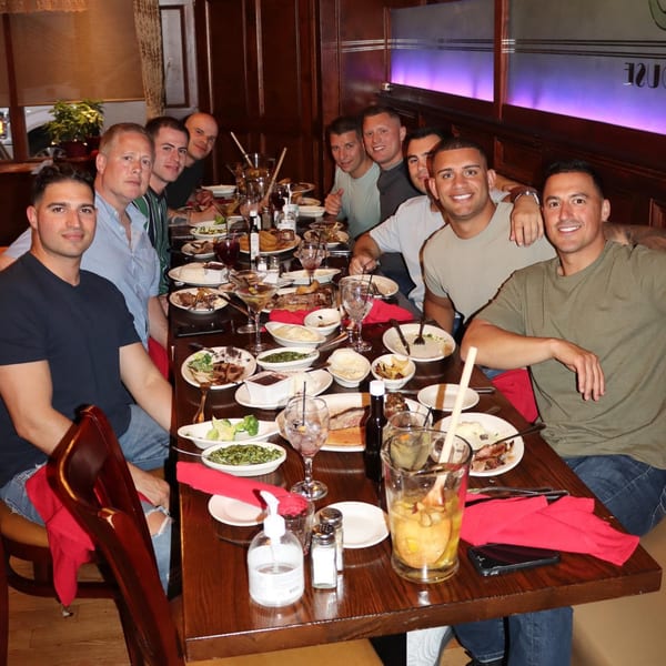 A group of men smiling at a long table filled with plates of steak and sides at 354 Steakhouse.