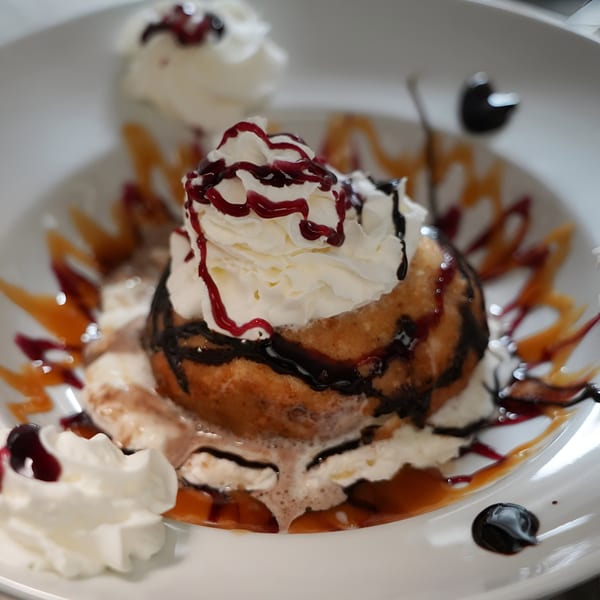 Fried ice cream dessert with whipped cream, chocolate, and berry drizzles on a white plate.
