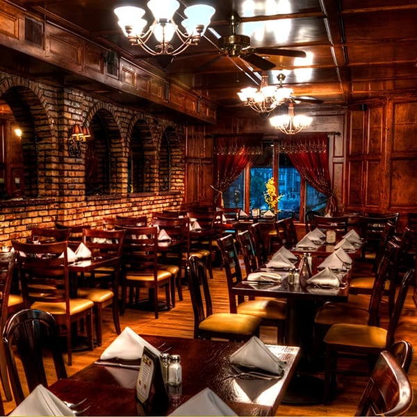 The 354 Steakhouse dining room features brick arches, wood paneling, chandeliers, and set tables.