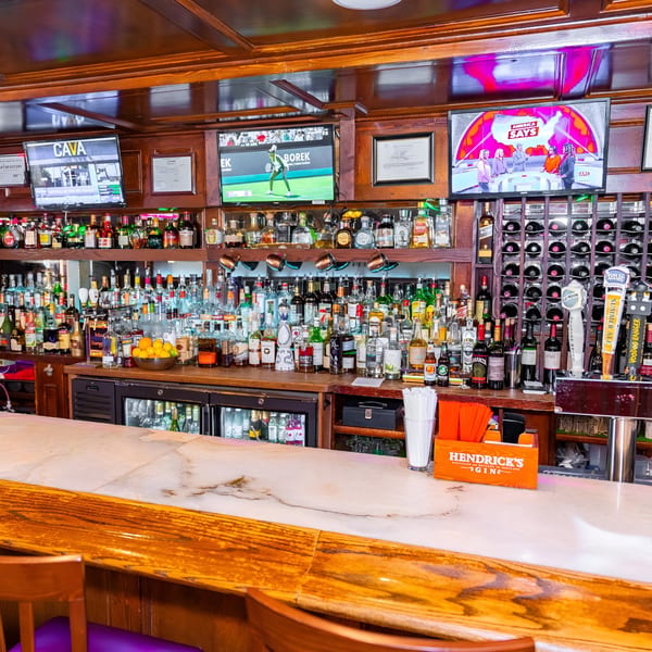 A well-stocked bar at 354 Steakhouse with various liquor bottles, beer taps, and TVs.